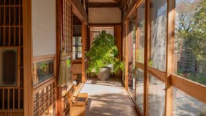 自然光が差し込む縁側の廊下で、木床と柱を整え再生された古民家の通路の様子。