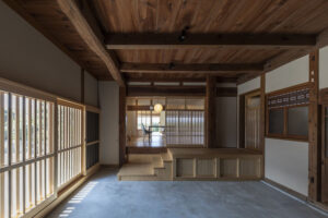 自然光が差し込む縁側の廊下を備え、木の梁や床材を活かして再生された古民家の室内空間。